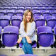 Dr. Joanna Fong-Isariyawongse sitting in a sports stadium seat
