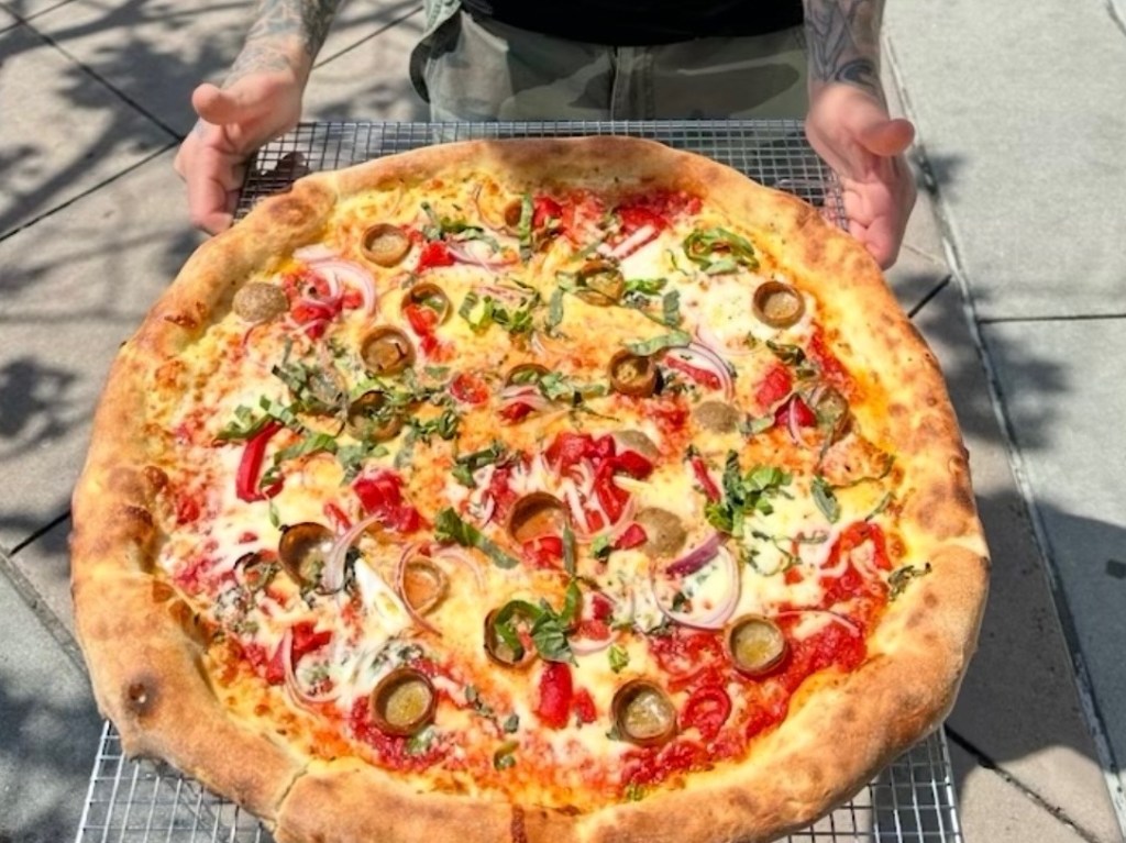 A large New York-style pizza on a wire rack.