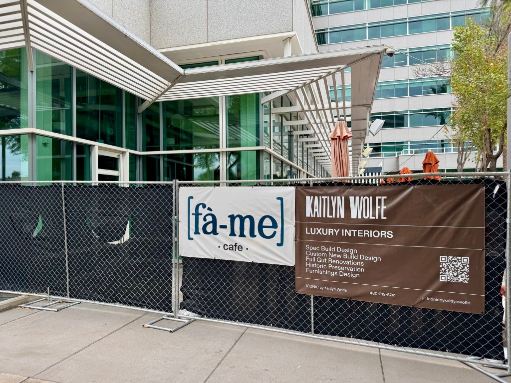 A banner advertising Fà-me Cafe hangs on a fence surrounding a vacant restaurant.