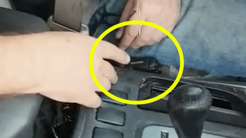 a yellow circle is drawn over an object wedged between the seat and center console of a car, with a man's hands nearby