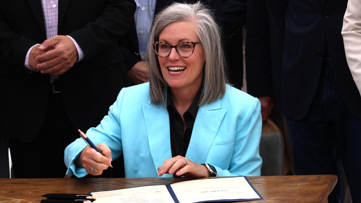 katie hobbs holds a pen while sitting at a desk and preparing to sign a bill