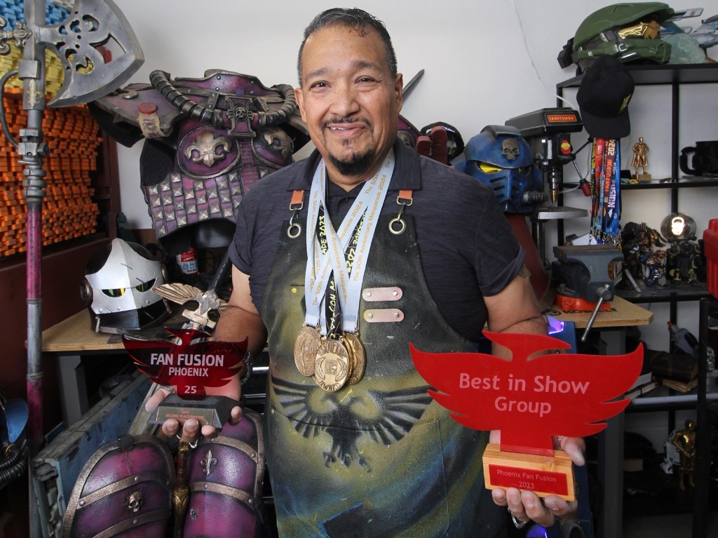 Phoenix "Warhammer" cosplayer Joe Ramirez in his workshop holding trophies he won at conventions.