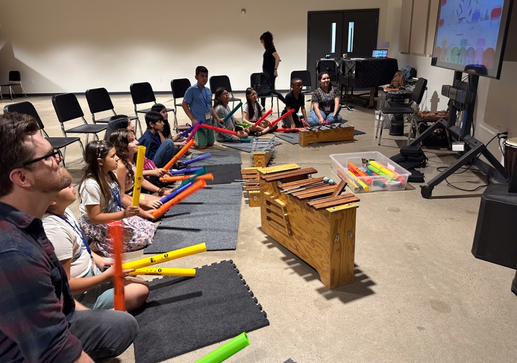 Children and adults use colorful percussion tubes and xylophone-style instruments during an interactive music workshop at Make Music Phoenix in 2025.