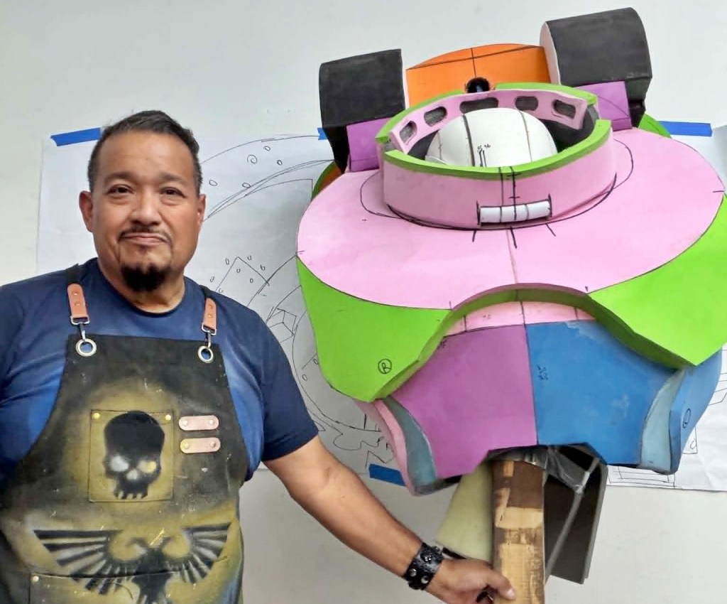 A man stands next to a "Warhammer 40K" cosplay armor he's building in his garage.