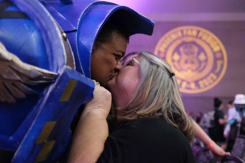 A man in a blue "Warhammer 40K" armor leans over to kiss his wife at Phoenix Fan Fusion.