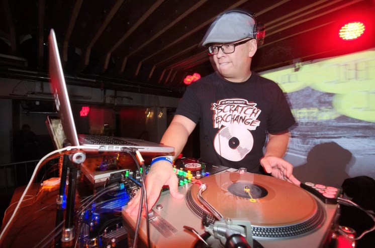 A Filipino man DJs on a pair of turntables in a nightclub.