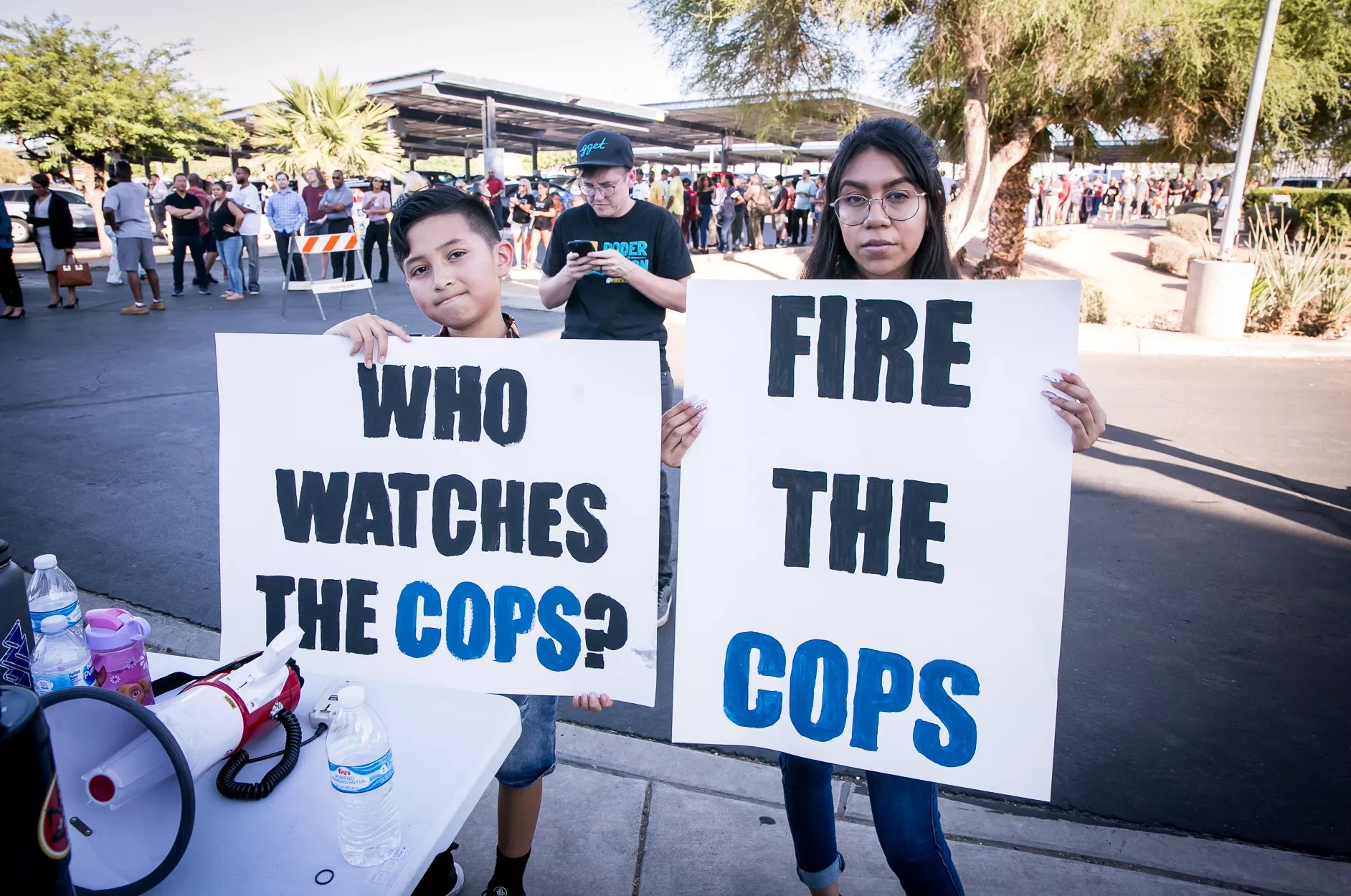 protesters with signs that say "Who watches the cops?" and "fire the cops"