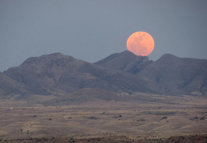 A full moon in the sky over mountains.