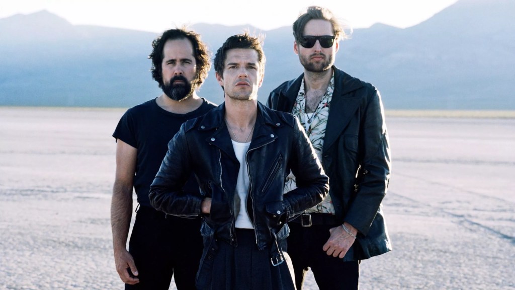 Three members of alt-rock band The Killers stand in the middle of the desert.