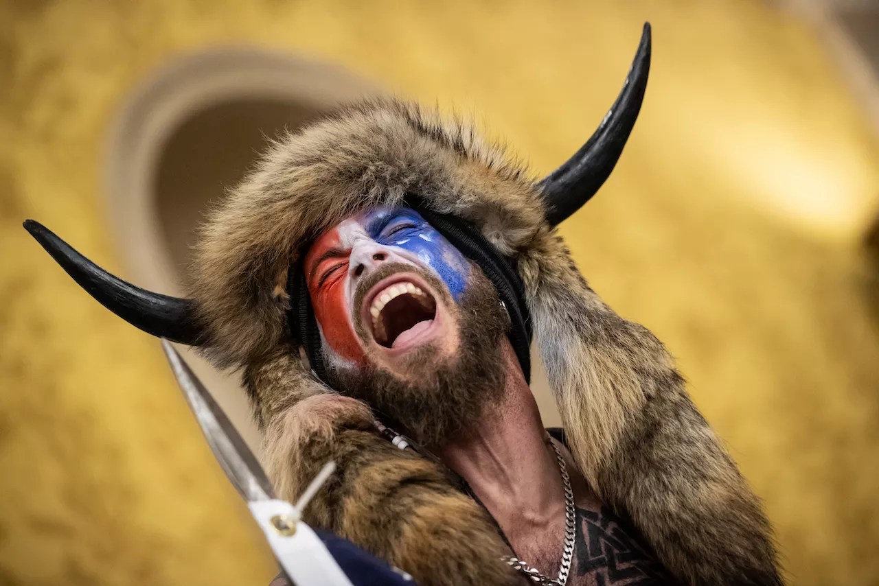 the qanon shaman, with a buffalo headdress and red-white-and-blue facepaint