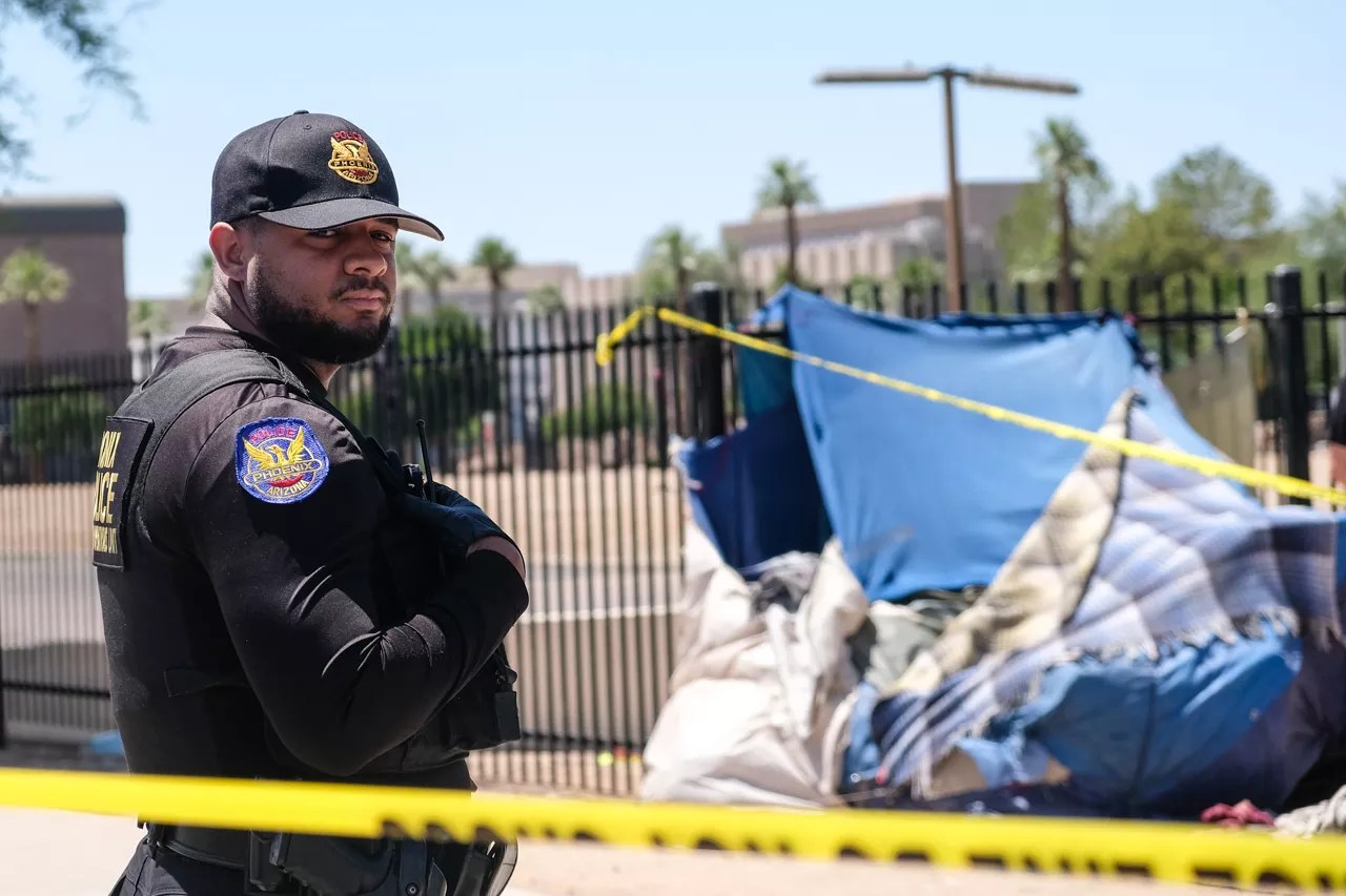 A Phoenix police officer stands in front of a tent belonging to an unhoused person