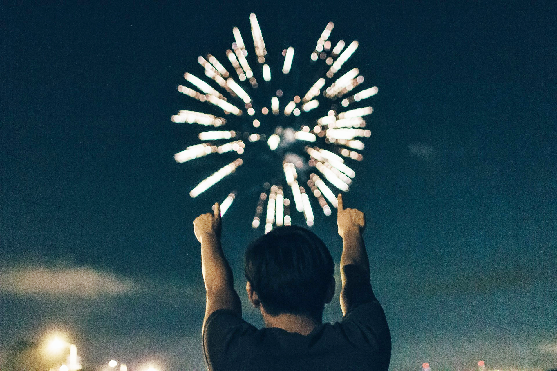 A boy point at an exploding firework in the sky with both hands.