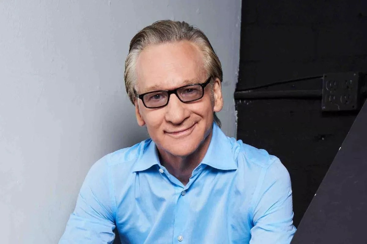 Bill Maher wearing a blue shirt and glasses.
