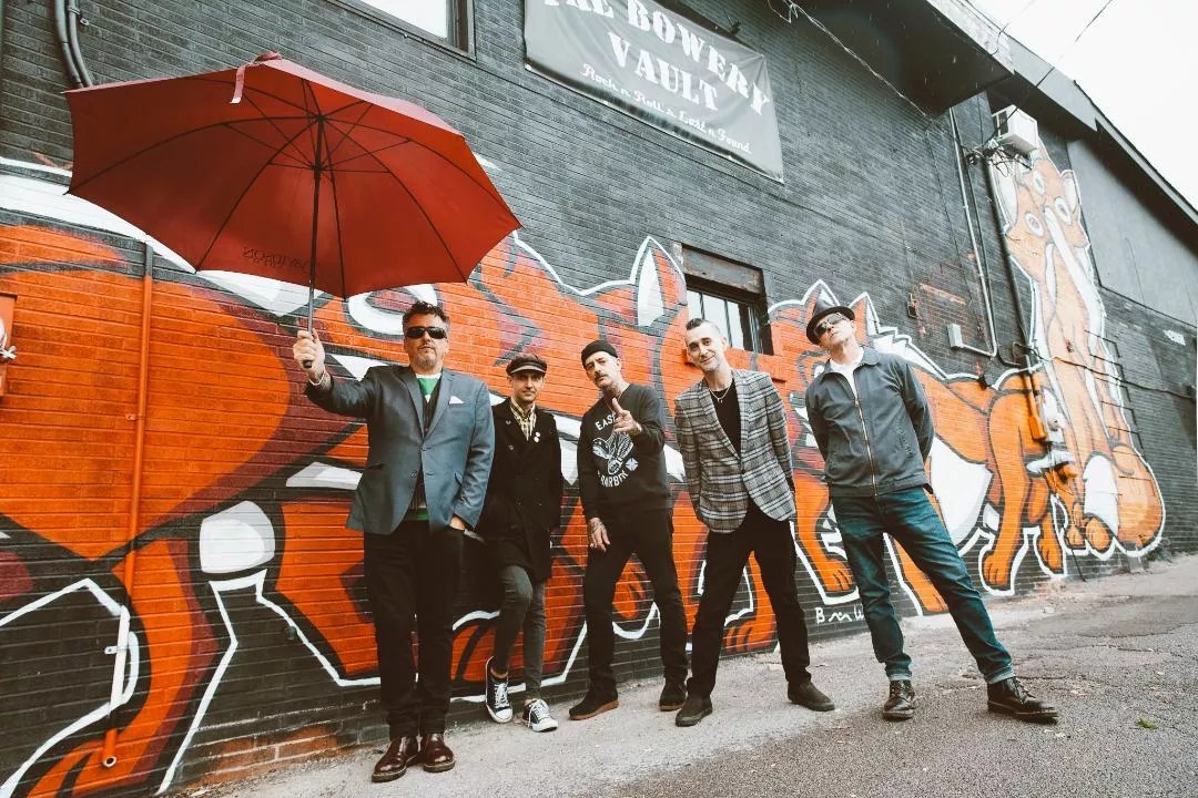 The band The Defiant stands against a wall.