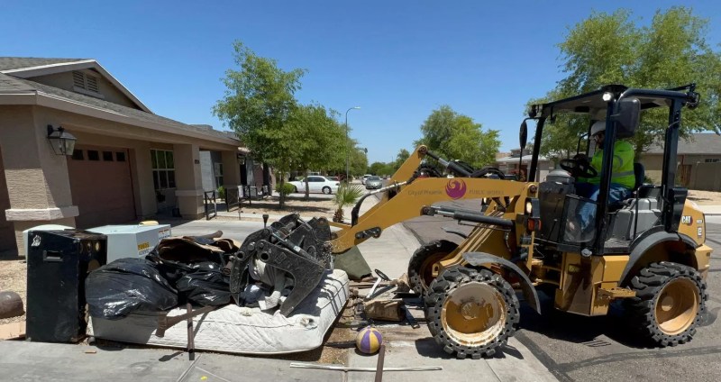A City of Phoenix backhoe loader scoops up debris on a residential curb.