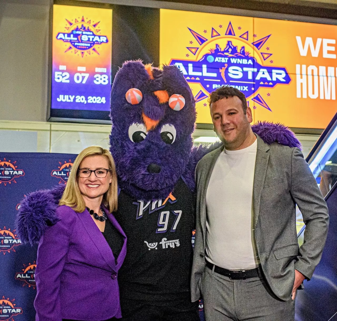A woman and a man pose for a photo with a person in a purple dragon costume.