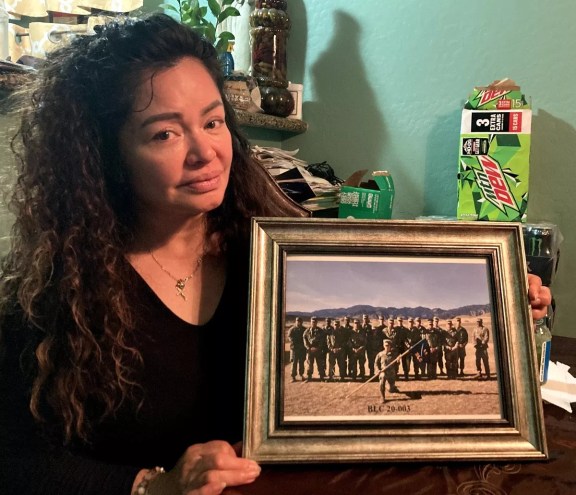 A woman holds a framed photo of soldiers.