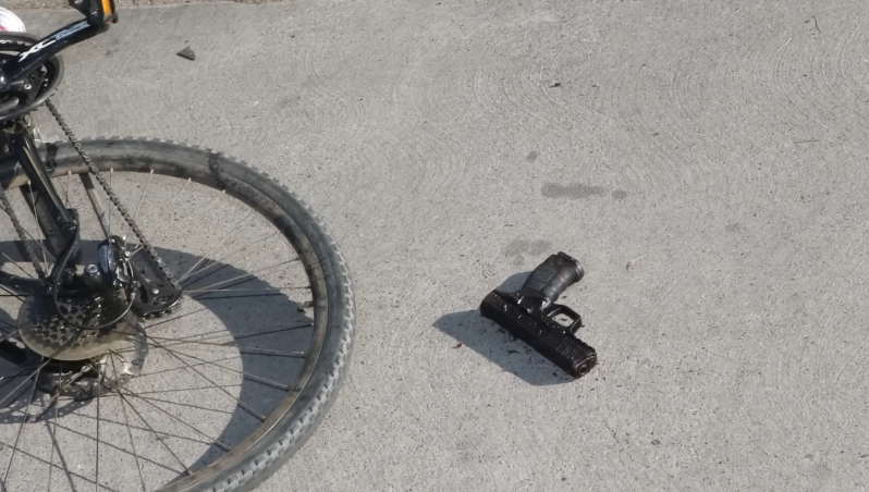 A wheel of a bicycle sits near a handgun on concrete.