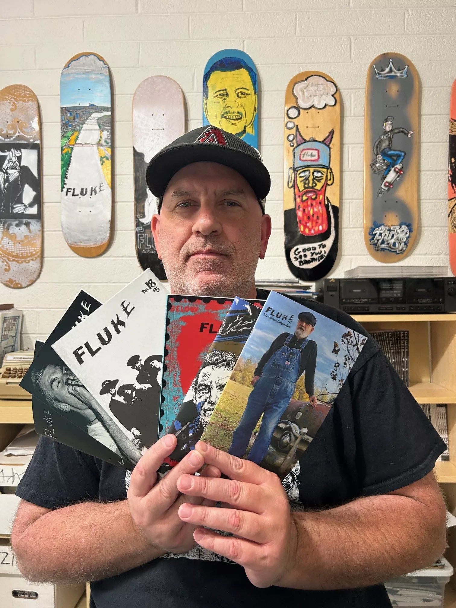 A man in a hat holding up a selection of zines.