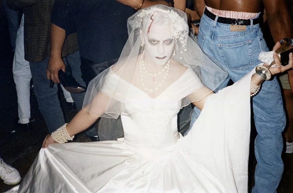 A man with a painted face wearing a white wedding dress.