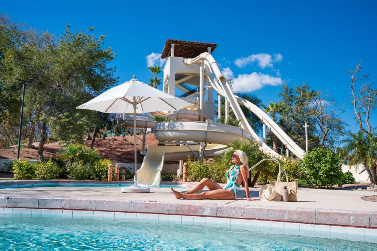 A woman sitting by a pool with a waterslide in the background.