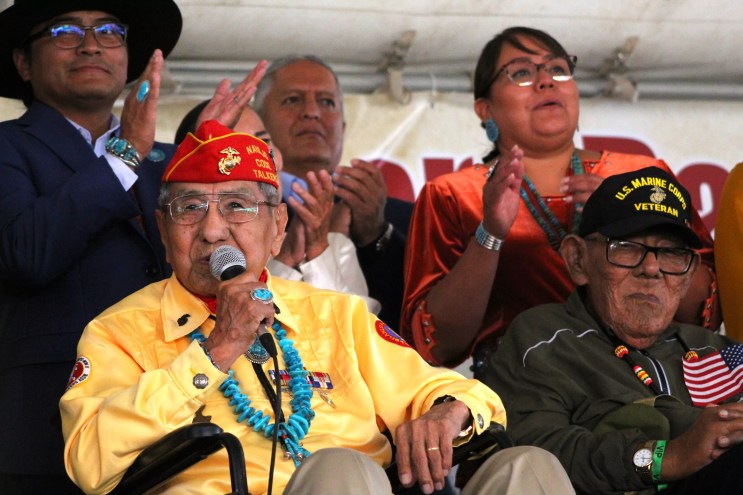 A man holds a microphone and speaks with people behind him.