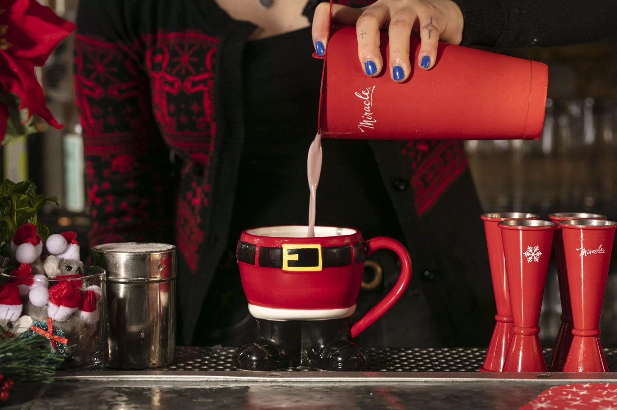 Miracle bartender pouring a cocktail into Santa-shaped glass.