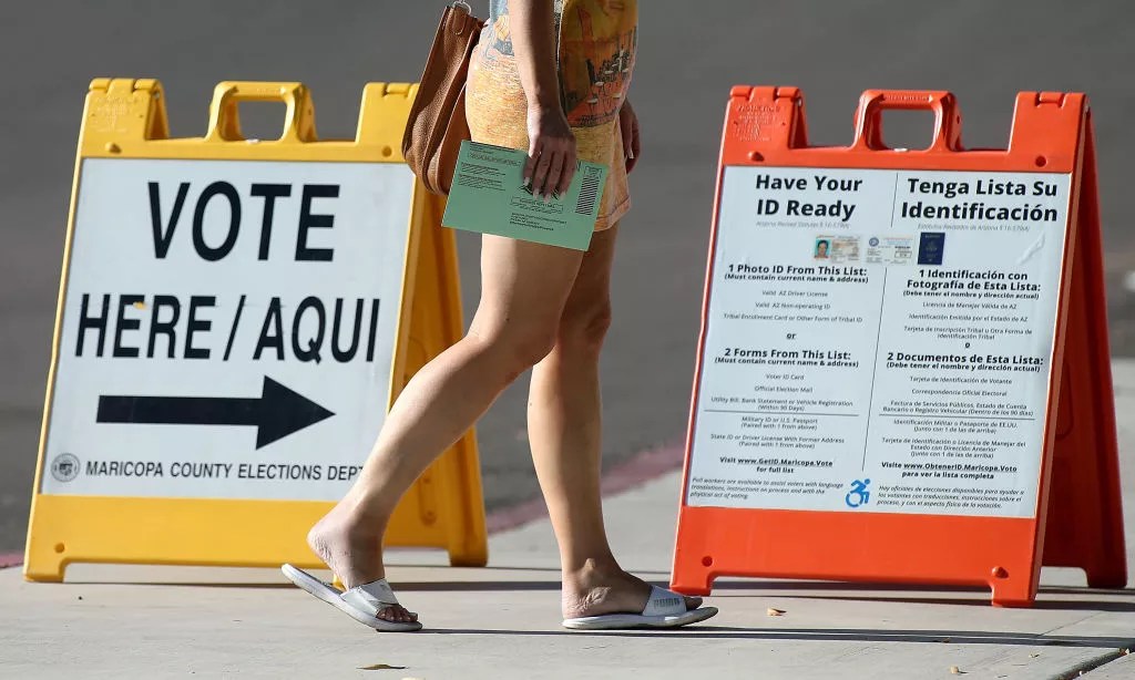 a person walks by a "VOTE" placard with a ballot