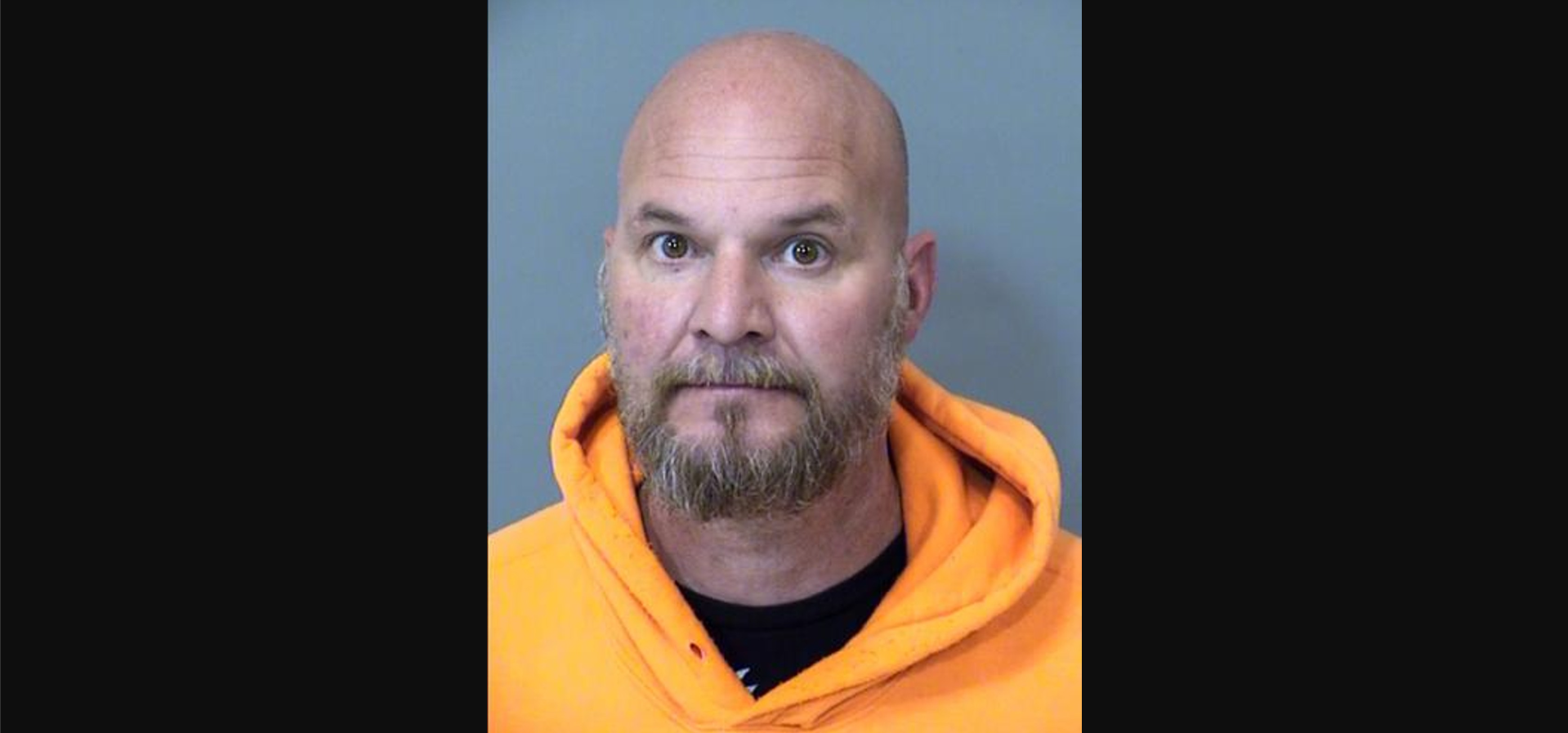 a bald man with a goatee in an orange hoodie seen in a mugshot