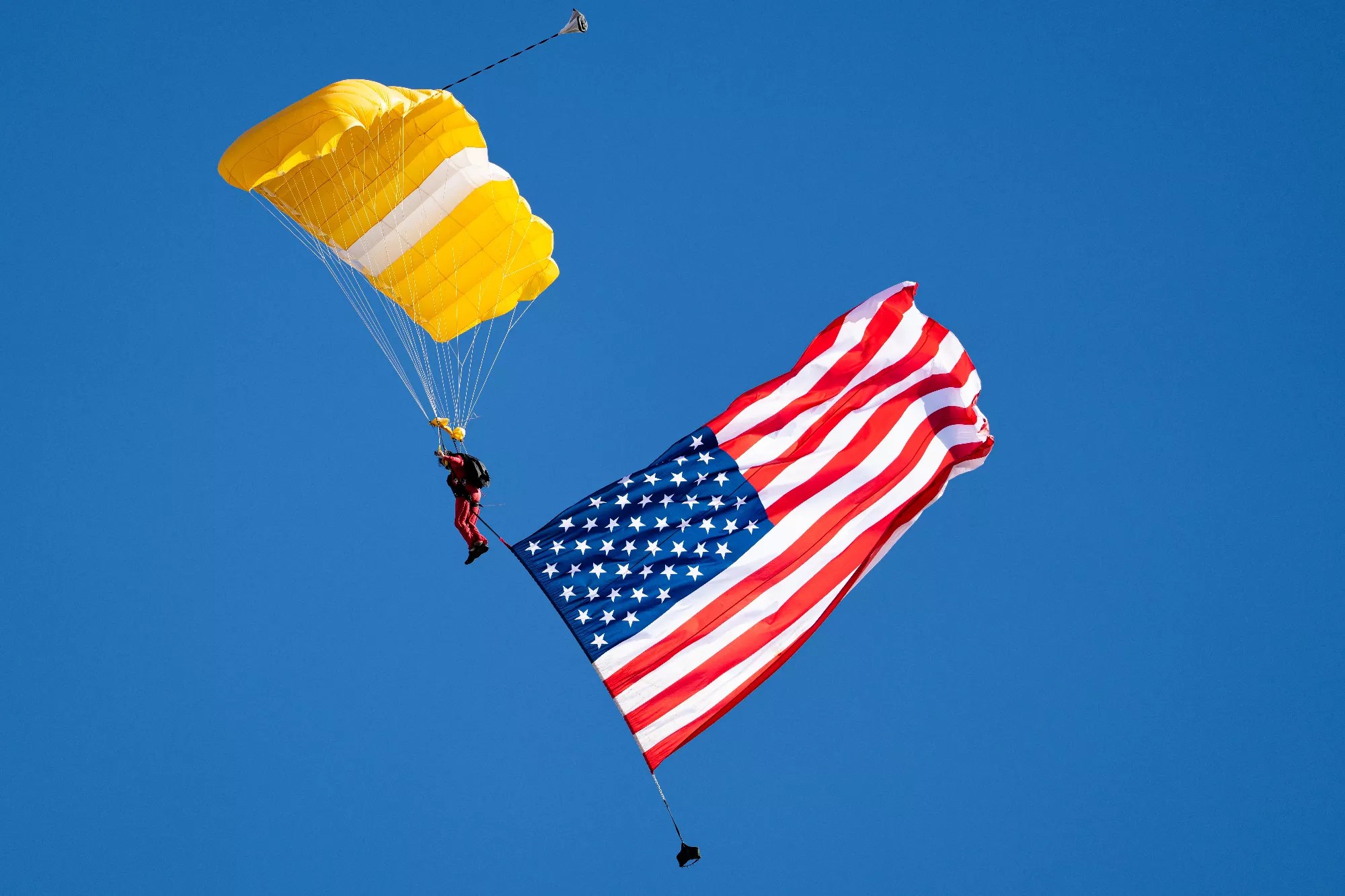 a skydiver with a yellow parachute and the American flag trailing below him