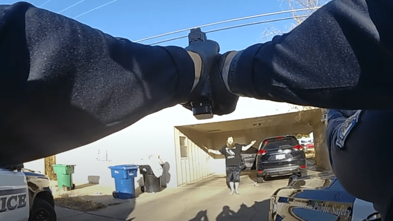 body-cam footage showing hands holding out a gun at a man who has his arms raised and a knife in one hand