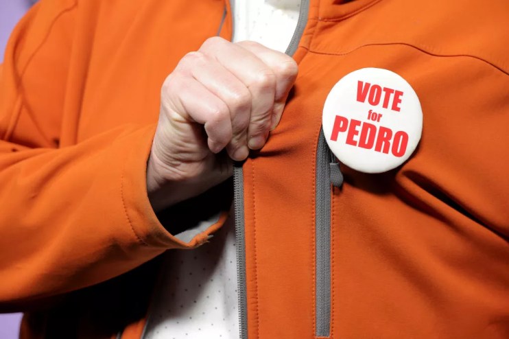 a hand grabs the lapel of an orange jacket that features a "vote for pedro" pin