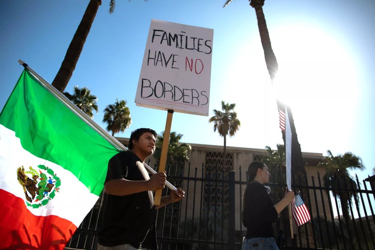 a protester holds a mexican flag and a sign that says" families have no borders"