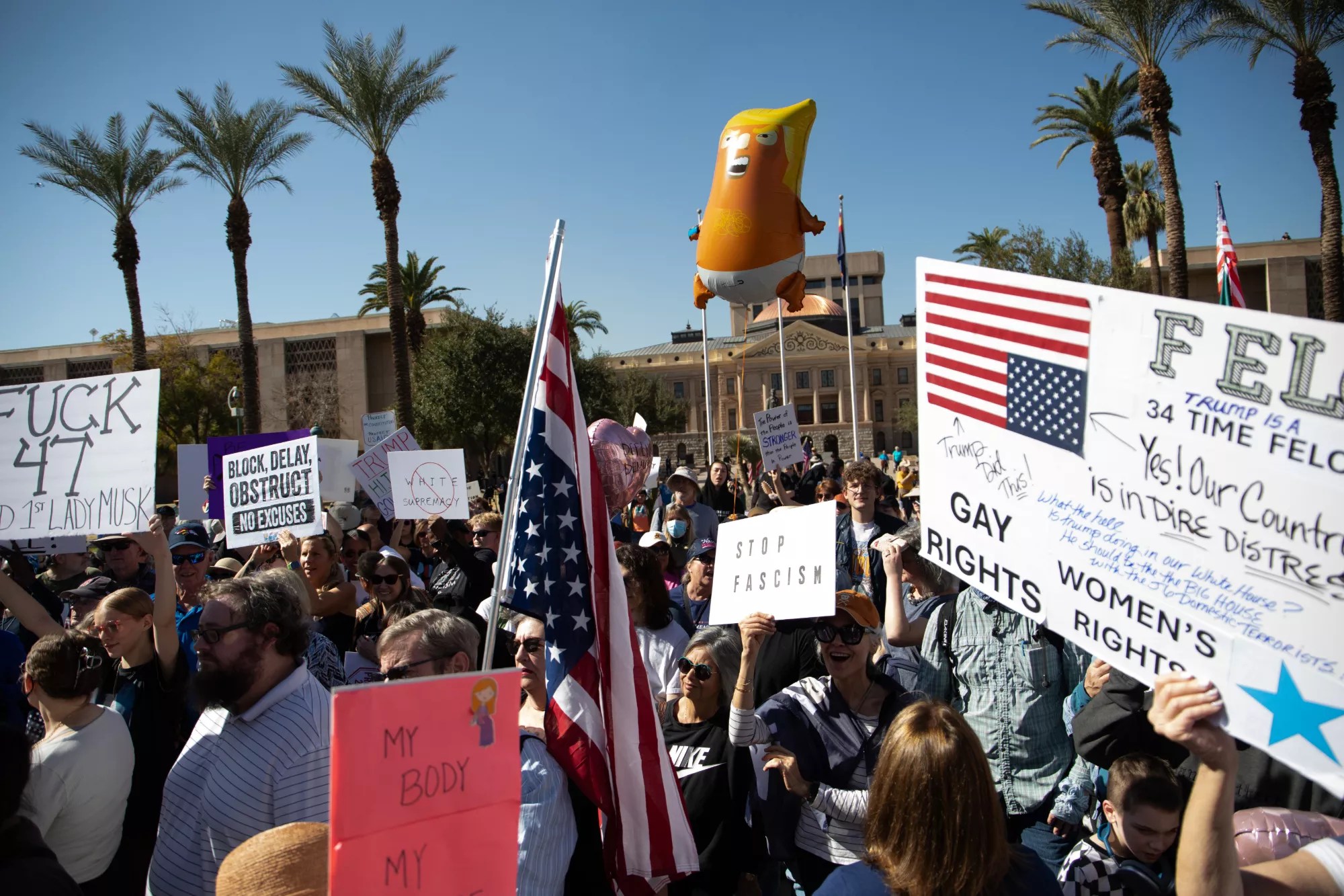 protesters with an inflatable donald trump baby balloon and signs that say "stop fascism"