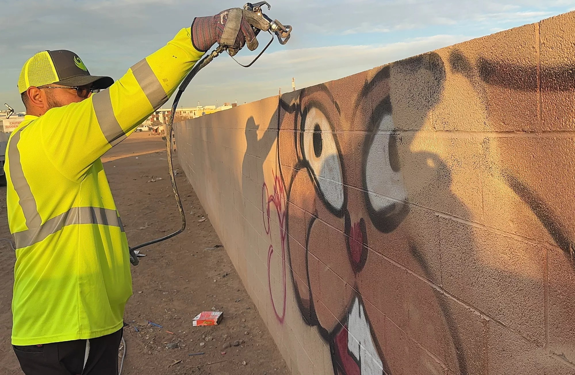 a man sandblasting graffiti off a block wall