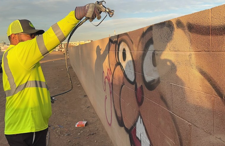 a man sandblasting graffiti off a block wall