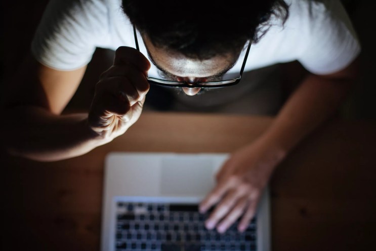 seen from above, a man touches his glasses while looking at a laptop
