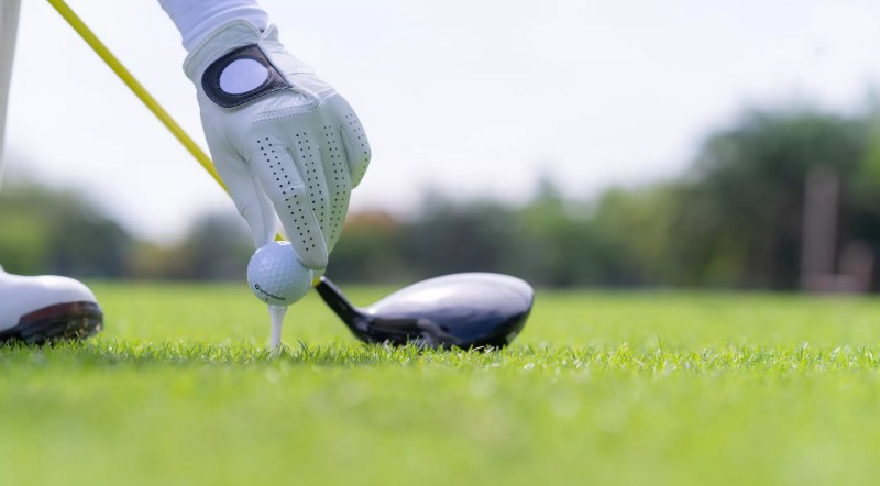 a gloved hand placing a ball on a tee in front of a golf club