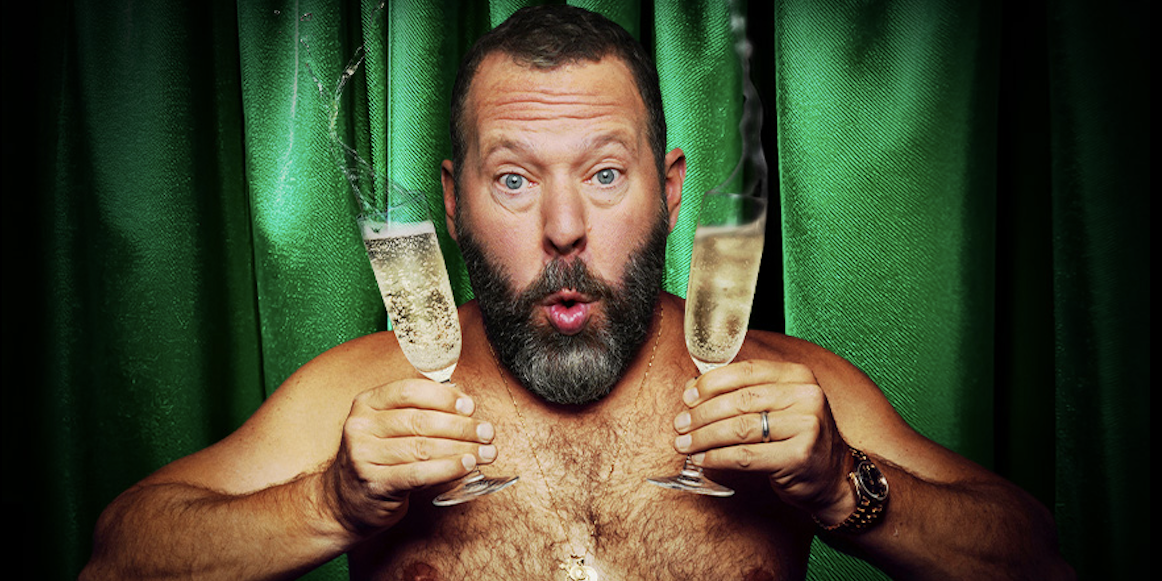 A shirtless man holding glasses of Champagne.