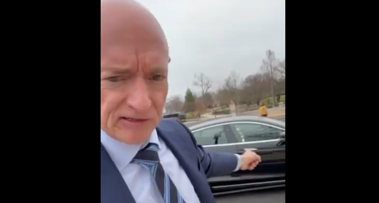 mark kelly points at a tesla behind him
