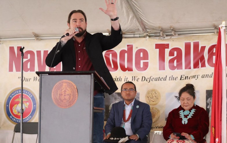eli crane speaks at a podium in front of a "navajo code talkers day" banner