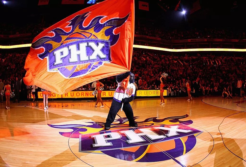 the suns gorilla mascot waving a suns flag on the court
