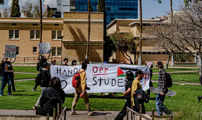 students hold up a banner that says "hands off our students" on asu's campus