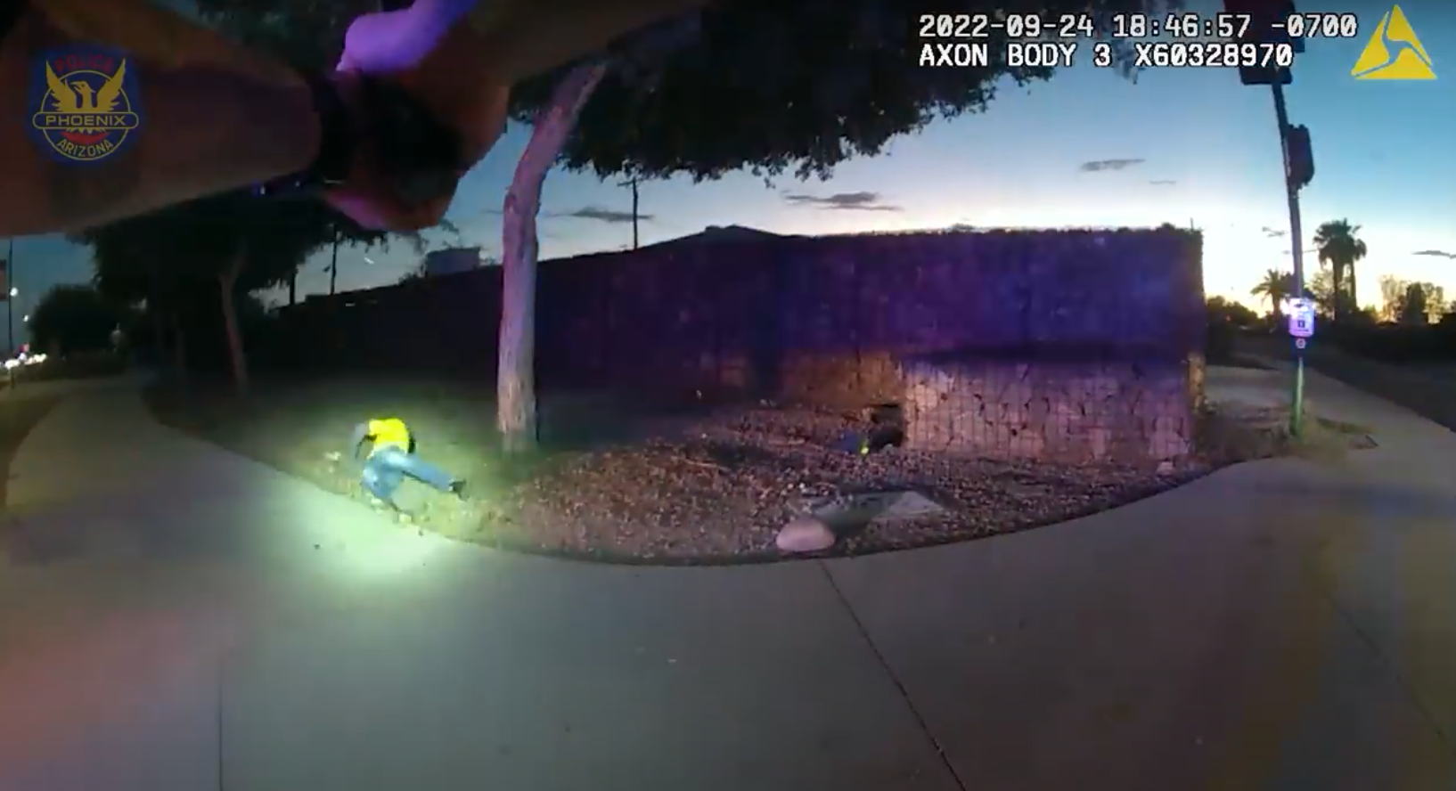body-cam footage showing hands pointing a gun at a figure in a yellow shirt on the ground
