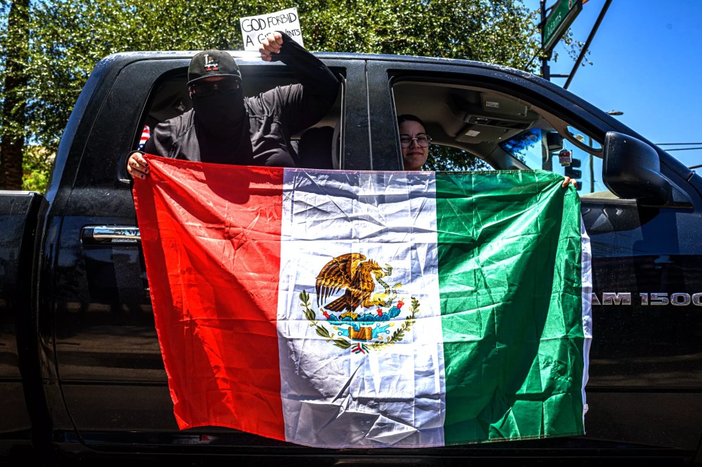 a masked protester holds a mexican flag outside of a pickup truck