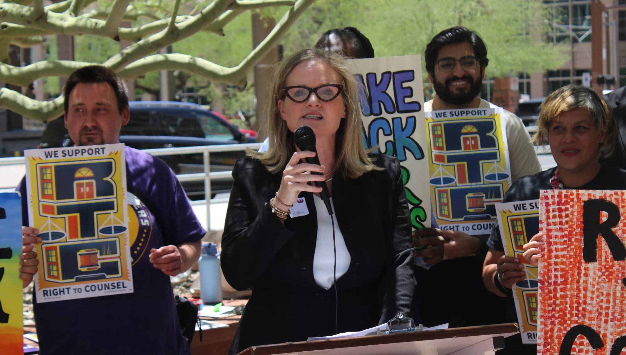 a woman in glasses speaks at a protest