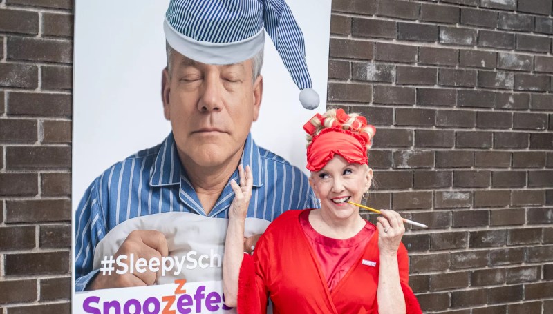 a woman stands by a poster of a sleeping david schweikert