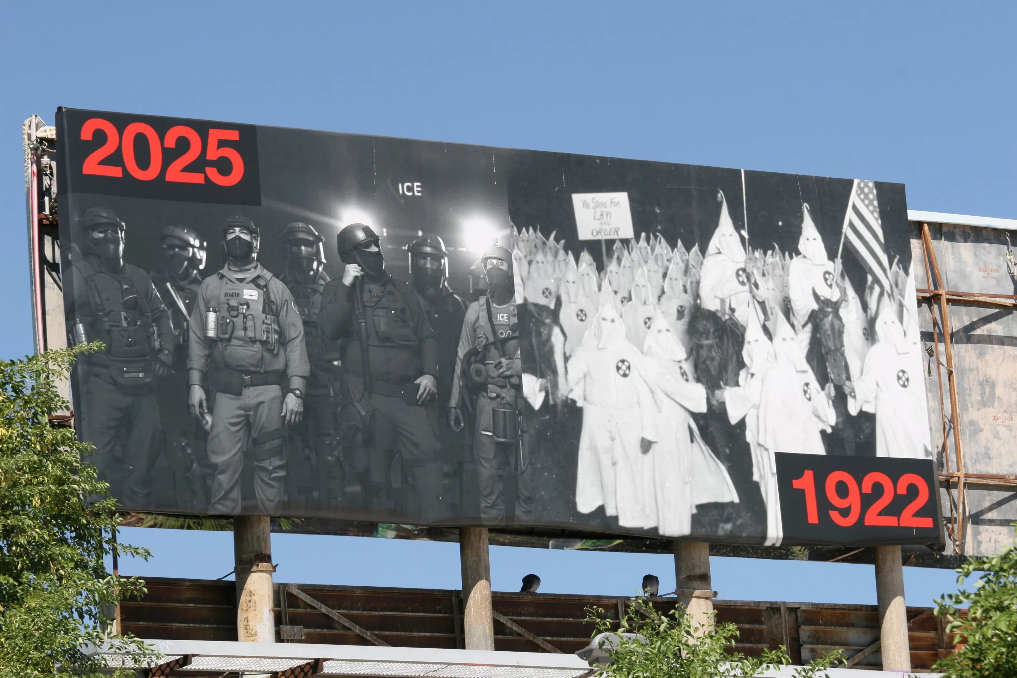 A billboard juxtaposes two large black-and-white photos: of ICE agents in 2025 and of a Klan rally in 1922